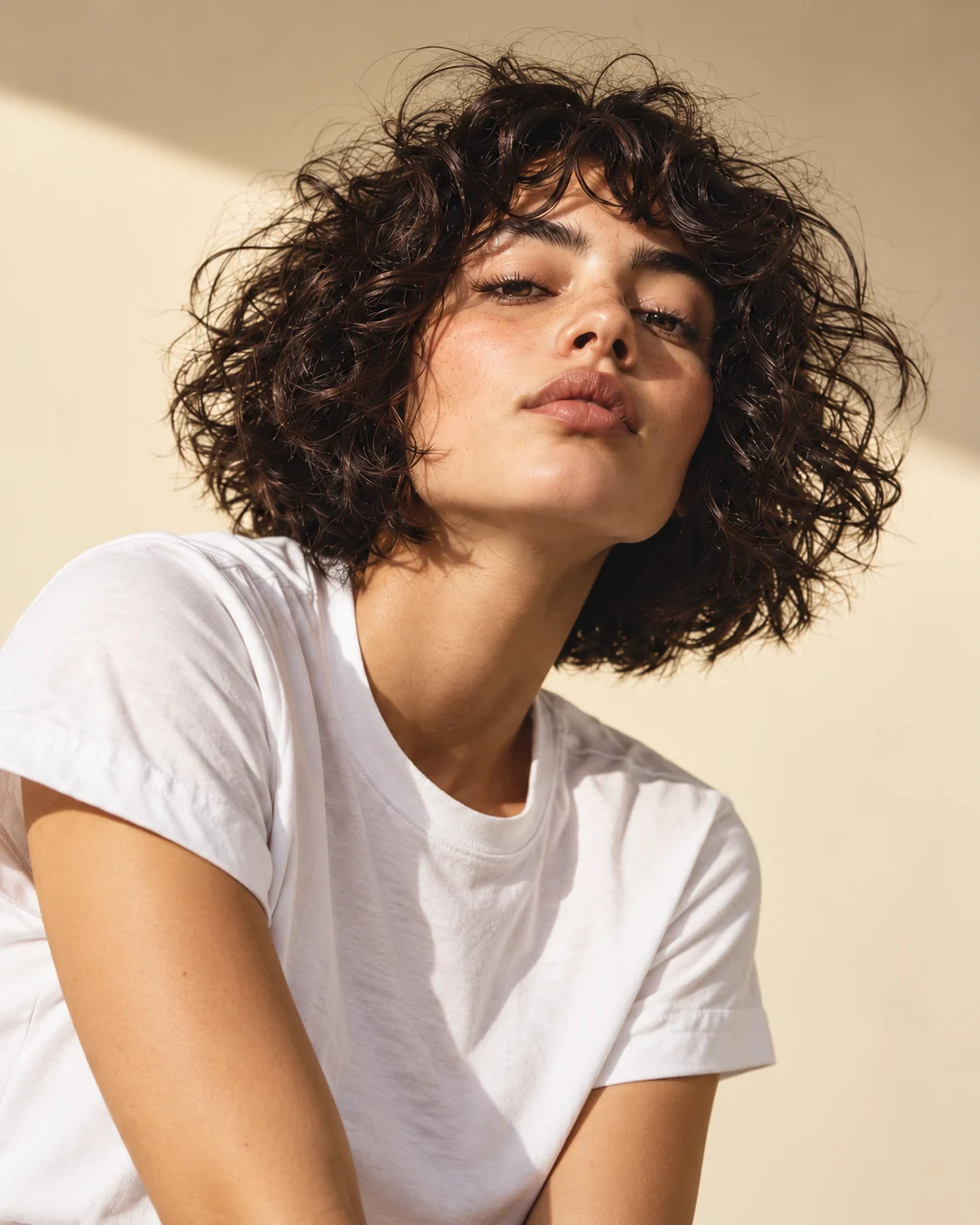 A dark curly bob with a bold shape, paired with a simple white tee.